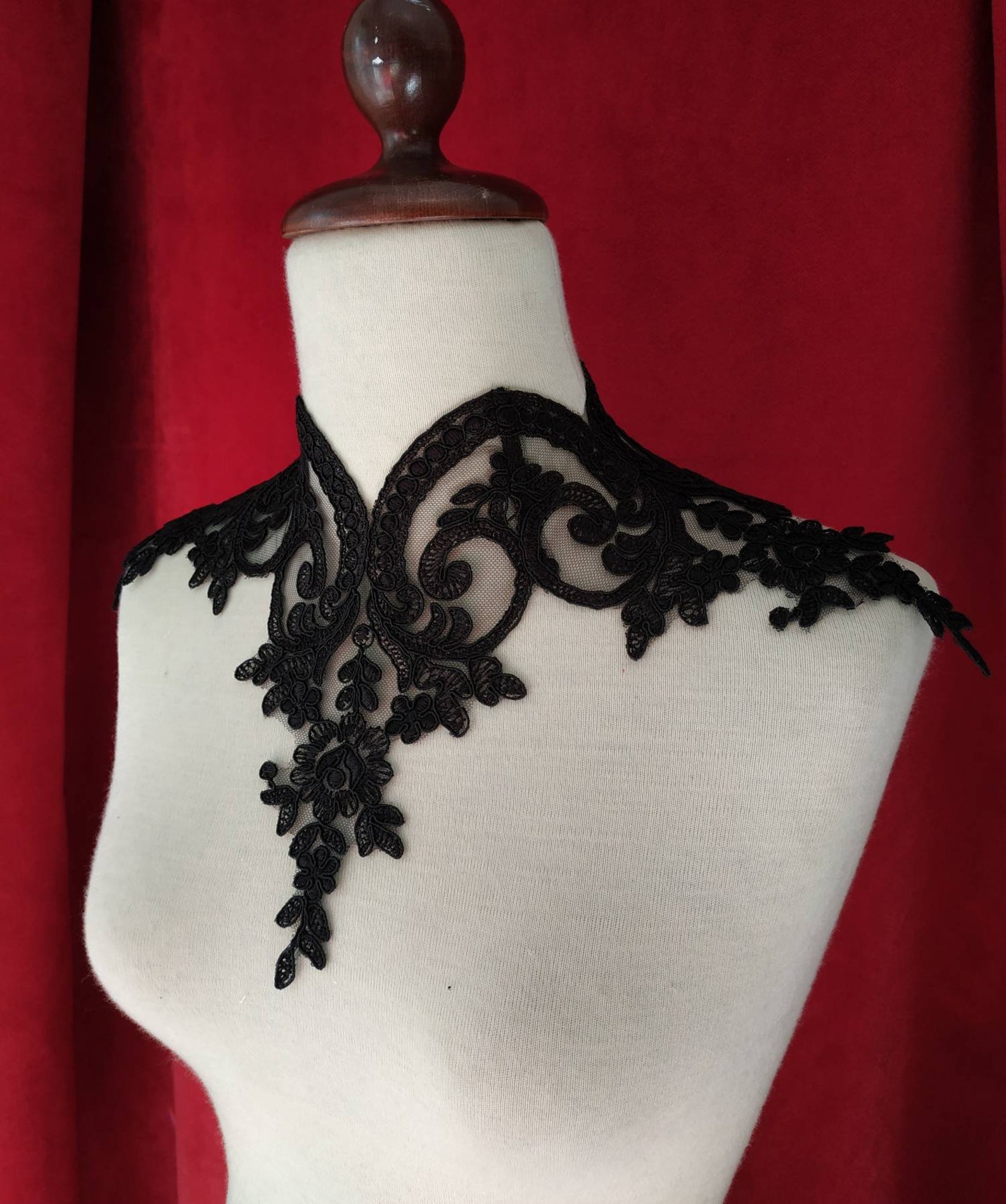Gothic black lace choker with floral embroidery on mannequin against deep red velvet background.
