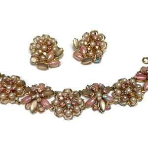 Könnte beinhalten: Ein Vintage-Schmuckset mit Armband und passenden Clip-Ohrringen. Das Set hat eine goldfarbene Metallbasis mit floralen Designs. Die Blumen sind mit Kunstperlen, rosa und irisierenden Strasssteinen verziert.