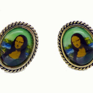 Può includere: Un paio di orecchini ovali dorati con un bordo a corda. Ogni orecchino presenta un cabochon di vetro con un'immagine stampata della Gioconda.