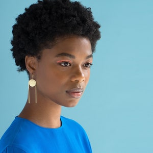 Black Woman in bright blue shirt with gold tone earrings on. Earrings made by L.Greenwalt Jewelry of Portland, OR.