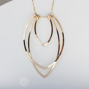 Gold large flame necklace on white arc prop. 
Made by L.Greenwalt Jewelry of Portland, OR.