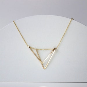 Geometric Gold Triangle necklace on white arc prop against soft white light background. 
Necklace made by L.Greenwalt Jewelry of Portland, OR.