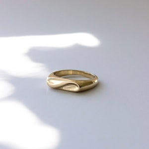 Gold Abstract infinity signet ring on soft white dappled light background. 
made by L.Greenwalt Jewelry of Portland, OR.