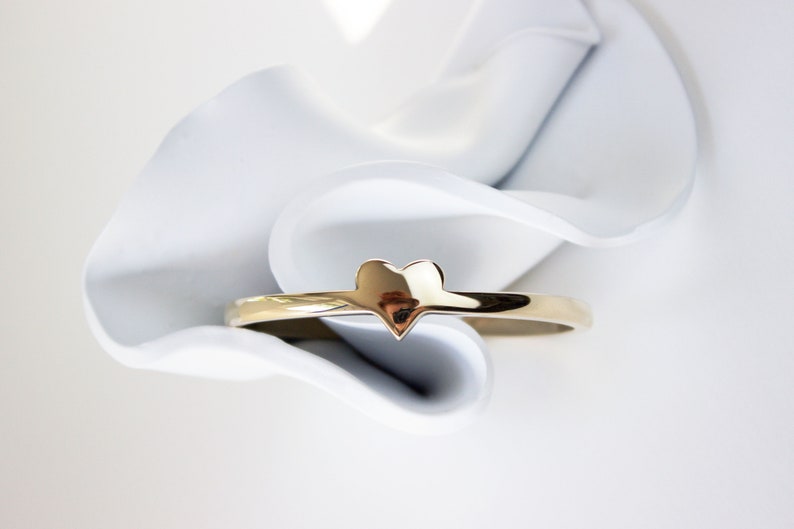 Puede incluir: Un anillo de oro en forma de coraz&oacute;n sobre un fondo blanco.