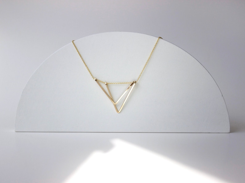 Geometric Gold Triangle necklace on white arc prop against soft white light background. 
Necklace made by L.Greenwalt Jewelry of Portland, OR.