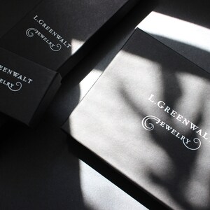 Puede incluir: Tres cajas negras con el texto "L. Greenwalt Jewelry" en letras blancas. Las cajas est&aacute;n apiladas una encima de la otra.