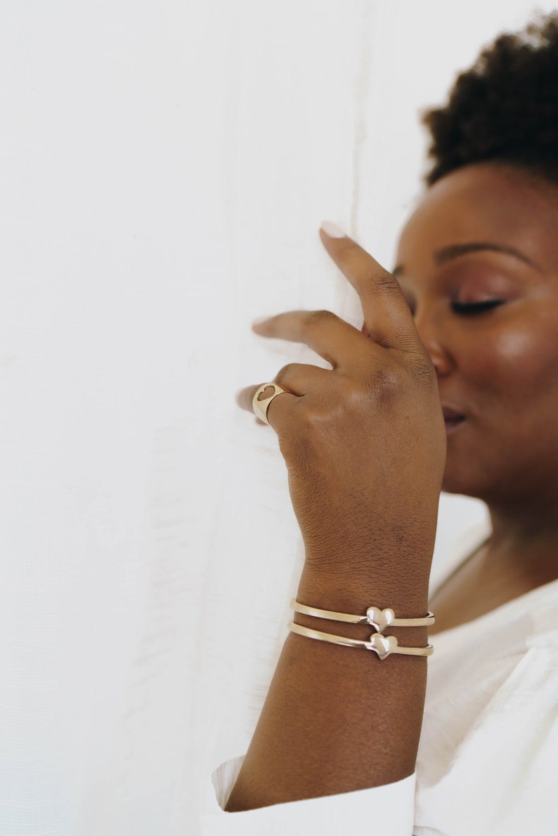 Puede incluir: Una persona lleva un anillo de oro en forma de coraz&oacute;n y dos pulseras de oro en forma de coraz&oacute;n en la mu&ntilde;eca.