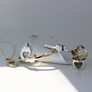 Puede incluir: Un conjunto de joyas de oro y plata con recortes en forma de coraz&oacute;n. El conjunto incluye un collar con un colgante, una pulsera y dos anillos.