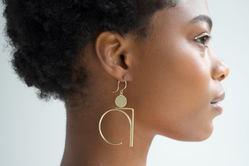 Black Woman in Abstract Gold Geometric Statement Earrings. 
Made by L.Greenwalt Jewelry of Portland, OR.