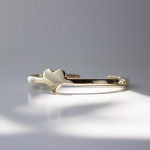 Puede incluir: Un brazalete de oro con un dije en forma de coraz&oacute;n. El brazalete est&aacute; hecho de un metal delgado y liso y tiene un dise&ntilde;o simple.