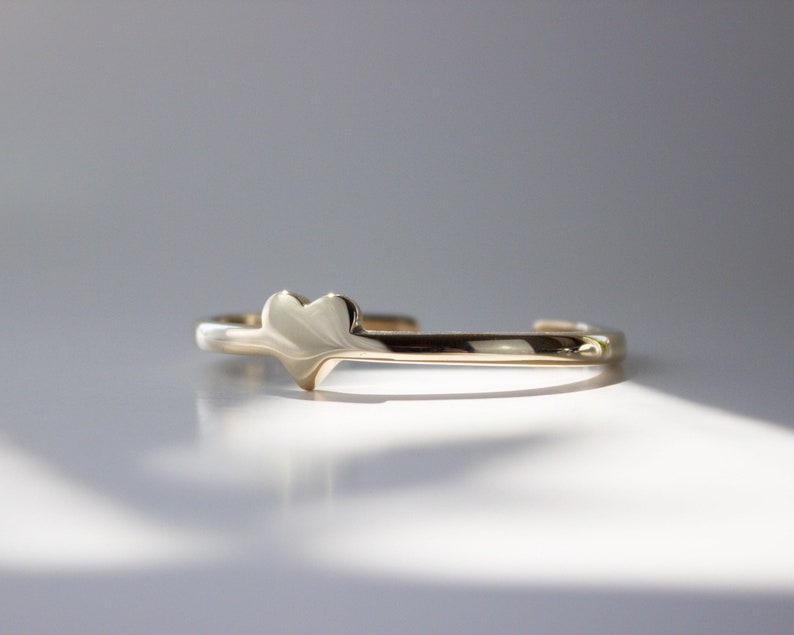 Puede incluir: Un brazalete de oro con un dije en forma de coraz&oacute;n. El brazalete est&aacute; hecho de un metal delgado y liso y tiene un dise&ntilde;o simple.