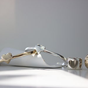 Puede incluir: Tres anillos de coraz&oacute;n de plata y oro. Dos de los anillos son delgados y tienen una forma de coraz&oacute;n en el lateral. El tercer anillo es m&aacute;s grueso y tiene un corte en forma de coraz&oacute;n.