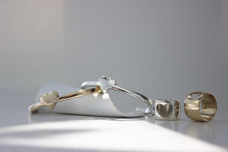 Puede incluir: Tres anillos de coraz&oacute;n de plata y oro. Dos de los anillos son delgados y tienen una forma de coraz&oacute;n en el lateral. El tercer anillo es m&aacute;s grueso y tiene un corte en forma de coraz&oacute;n.