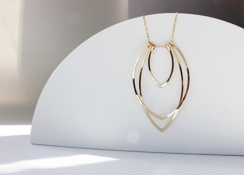 Gold large flame necklace on white arc prop. 
Made by L.Greenwalt Jewelry of Portland, OR.