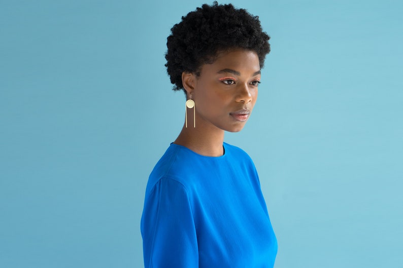 Black Woman in bright blue shirt with gold tone earrings on. Earrings made by L.Greenwalt Jewelry of Portland, OR.