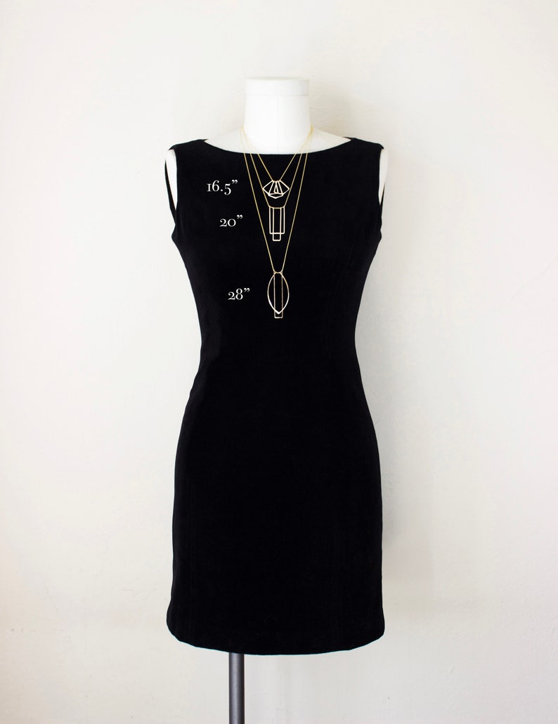 May include: A black sleeveless dress on a mannequin with three gold necklaces of varying lengths. The necklaces are 16.5", 20", and 28" long, each with a unique geometric pendant. The mannequin is set against a white background.