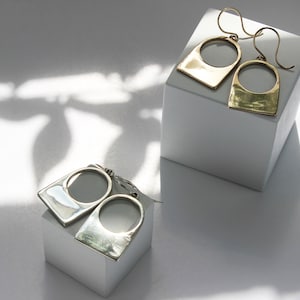 Art Deco Gold and Silver Lock Shape Pendant earrings on soft shadowed dappled light background. 
Made by L.Greenwalt Jewelry of Portland, OR.