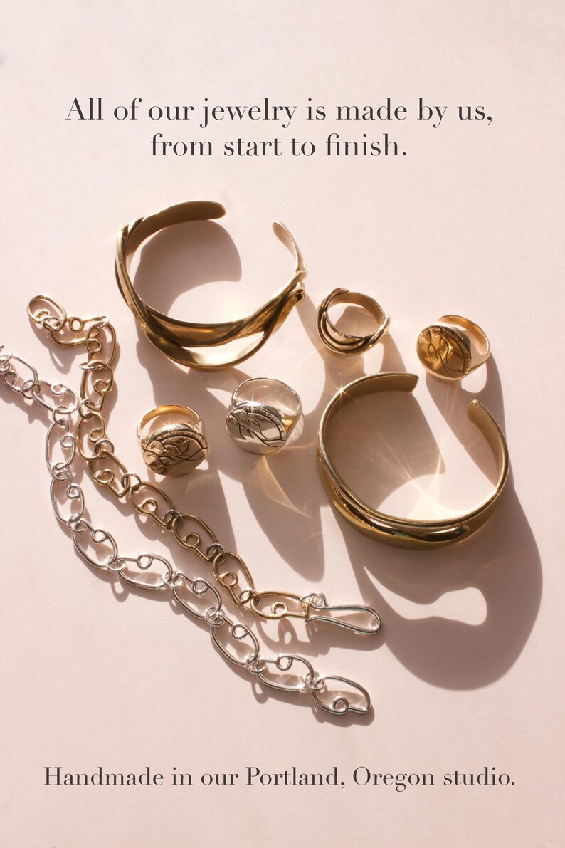 May include: An assortment of gold and silver jewelry, including rings, bracelets, and a chain necklace, is displayed on a light pink surface. The text "All of our jewelry is made by us, from start to finish" and "Handmade in our Portland, Oregon studio" are also visible.