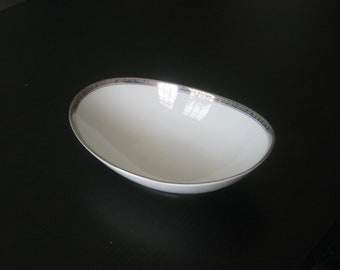 May include: A white oval serving bowl with a silver rim. The bowl is empty and sitting on a black surface.