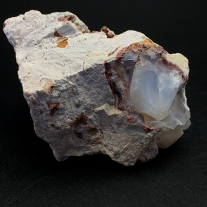 May include: A rough, white rock with a large, translucent, light blue opal embedded in it. The rock has reddish-brown veins and a few small, orange-brown inclusions.