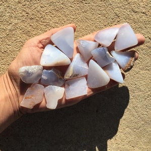 May include: A collection of blue chalcedony stones, some with a triangular shape, others with irregular shapes, in a hand.