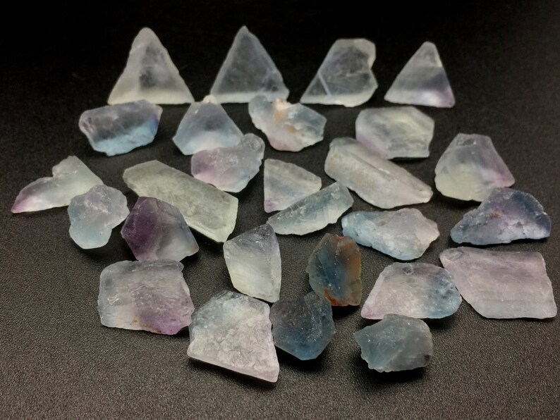 May include: A collection of fluorite crystals in various shades of blue, purple, and green. The crystals are rough and have a natural, unpolished look.