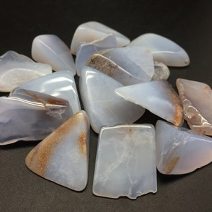 May include: A collection of blue chalcedony tumbled stones with brown inclusions. The stones are various shapes and sizes.