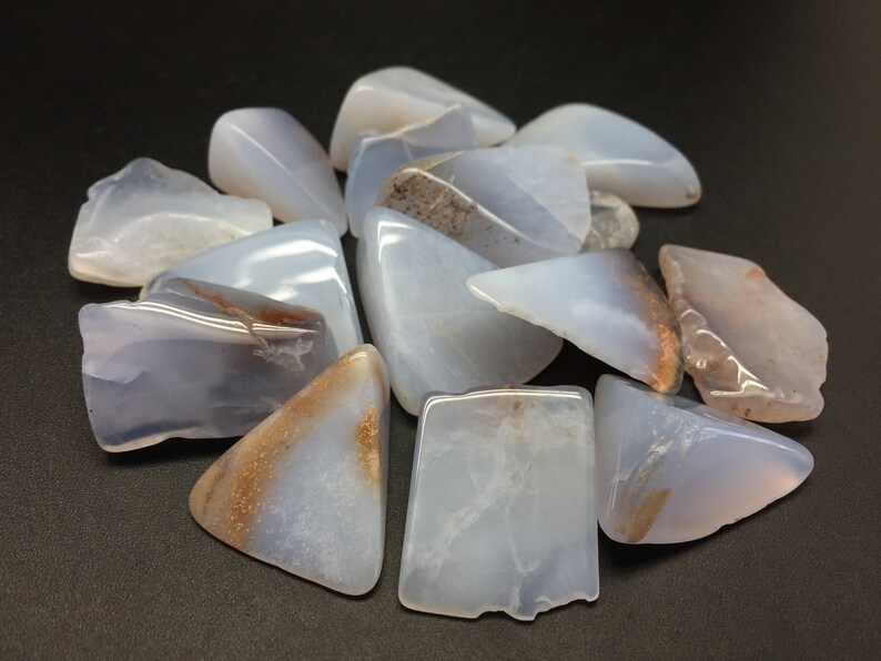 May include: A collection of blue chalcedony tumbled stones with brown inclusions. The stones are various shapes and sizes.