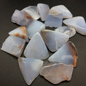 May include: A collection of blue lace agate stones, each with a unique shape and pattern of brown and white markings. The stones are smooth and polished, with a translucent appearance.