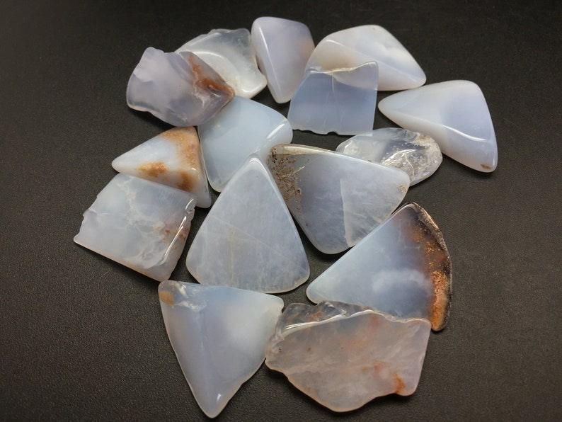 May include: A collection of blue lace agate stones, each with a unique shape and pattern of brown and white markings. The stones are smooth and polished, with a translucent appearance.