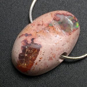 Op de afbeelding: Een ovale roze en witte opaal hanger met iriserende kleurvlekken, hangend aan een zilveren ketting.