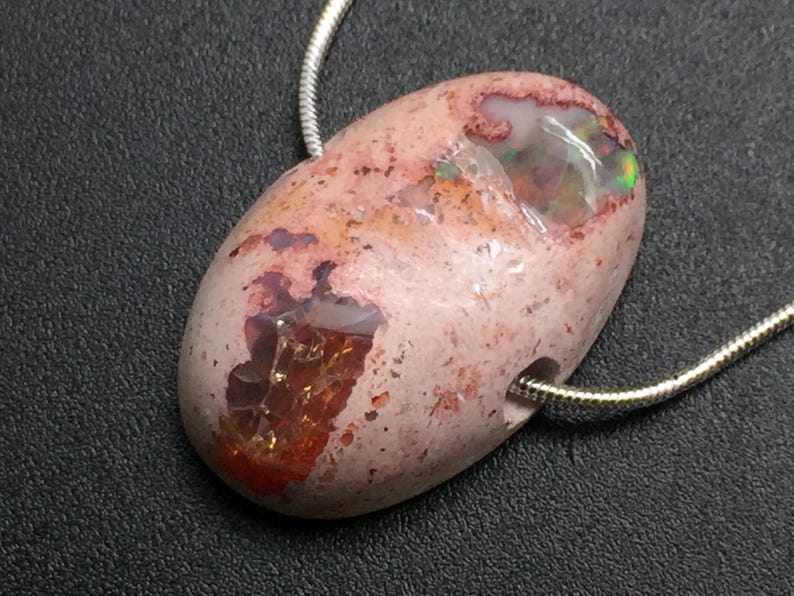 Op de afbeelding: Een ovale roze en witte opaal hanger met iriserende kleurvlekken, hangend aan een zilveren ketting.