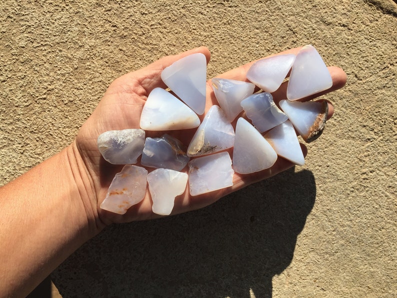 May include: A collection of blue chalcedony stones, some with a triangular shape, others with irregular shapes, in a hand.