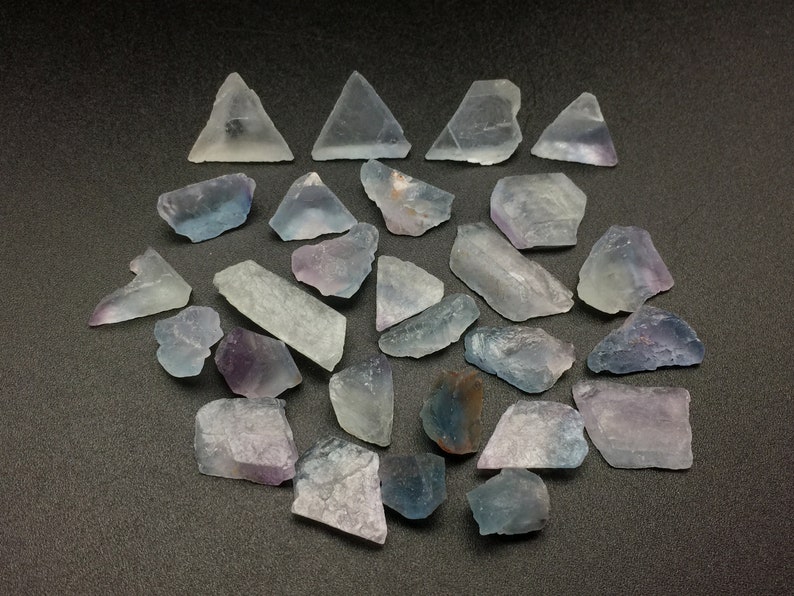 May include: A collection of 20 fluorite crystals in various shades of purple, blue, and clear. The crystals are rough and have a natural, unpolished look.