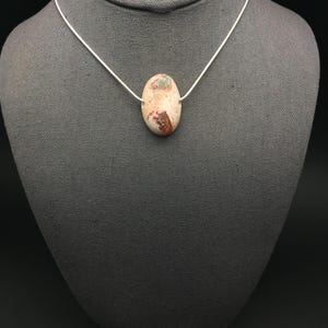 Op de afbeelding: Een zilveren ketting met een ovale hanger in lichtbruin met een mix van wit, bruin en groen.