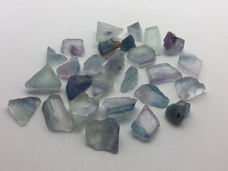 May include: A collection of small, rough, blue, green, and purple fluorite crystals. The crystals are various shapes and sizes.