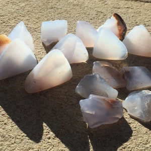May include: A collection of 14 smooth, translucent, light blue and white agate stones with brown and white banding. The stones are irregularly shaped and have a natural, polished finish.