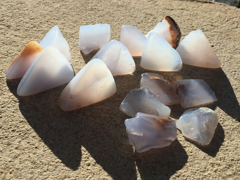 May include: A collection of 14 smooth, translucent, light blue and white agate stones with brown and white banding. The stones are irregularly shaped and have a natural, polished finish.