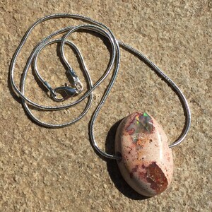 Op de afbeelding: Een zilveren ketting met een ovale hanger van roze en bruine opaal.