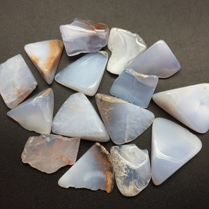 May include: A collection of 14 blue chalcedony crystal points with brown and white inclusions. The crystals are arranged in a circle on a black background.