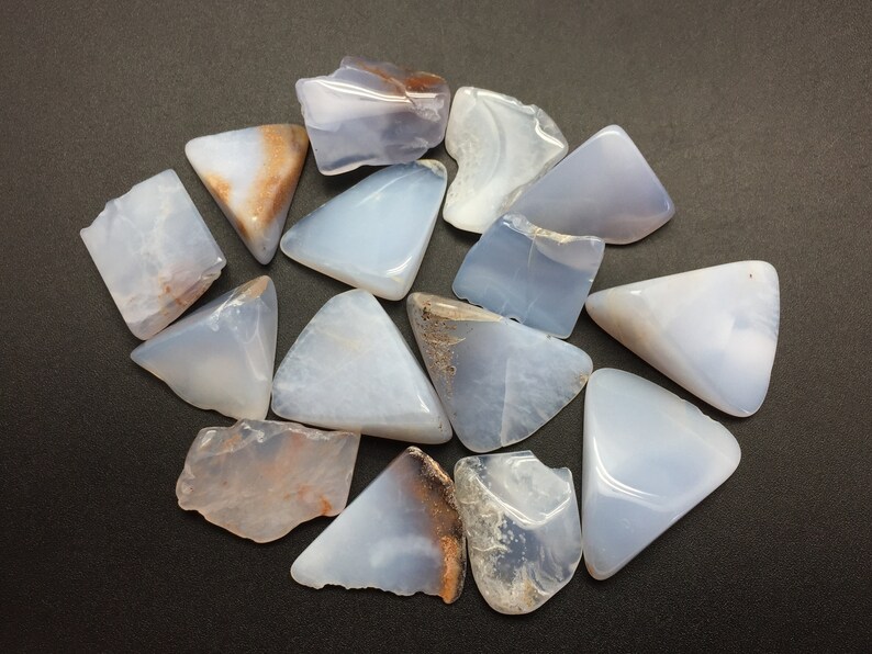 May include: A collection of 14 blue chalcedony crystal points with brown and white inclusions. The crystals are arranged in a circle on a black background.