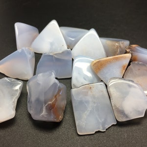 May include: A collection of blue lace agate stones, some with brown markings, in various shapes and sizes. The stones are smooth and polished.
