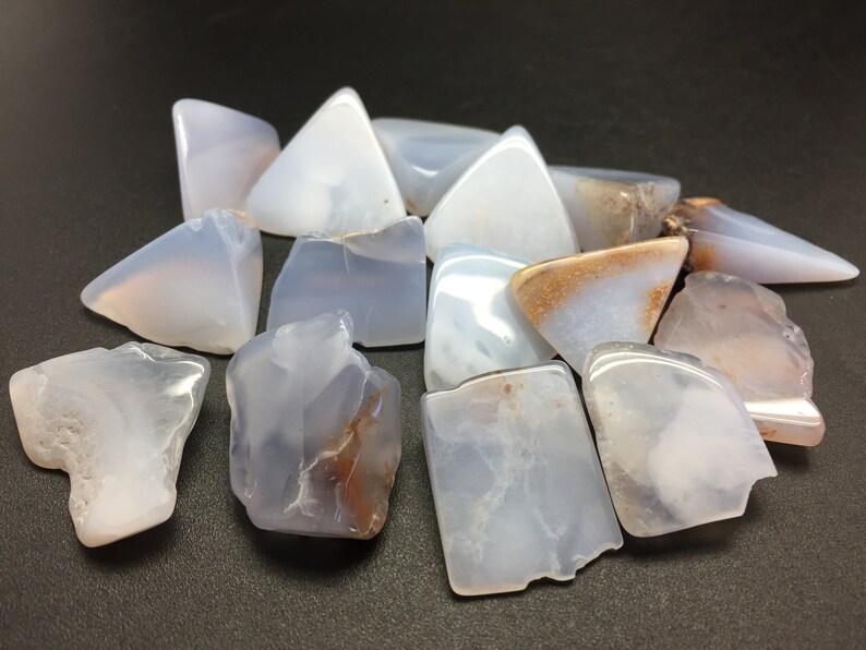May include: A collection of blue lace agate stones, some with brown markings, in various shapes and sizes. The stones are smooth and polished.
