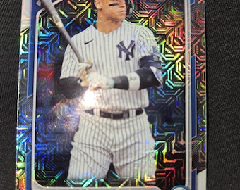 May include: Baseball card featuring Aaron Judge of the New York Yankees. The card has a blue and silver holographic design around the edges and a photo of Judge in his uniform holding a bat. The card also has the Bowman Chrome logo.