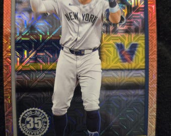 May include: A baseball card featuring Aaron Judge of the New York Yankees in his gray uniform. The card has a holographic background and the text "Yankees" and "Aaron Judge". The card commemorates the 35th anniversary.