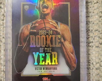 May include: A Topps Now Rookie of the Year card featuring Victor Wembanyama of the San Antonio Spurs. The card has a holographic finish and features a close-up of Wembanyama holding a basketball.
