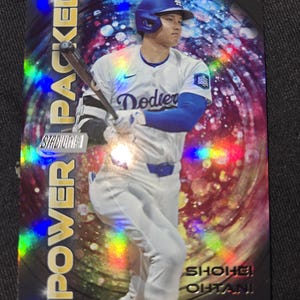 May include: A baseball card featuring Shohei Ohtani in a Dodgers uniform, holding a bat. The card has a holographic background with the words "POWER PACKED" and "STADIUM CLUB" on the left side. The player's name is at the bottom.