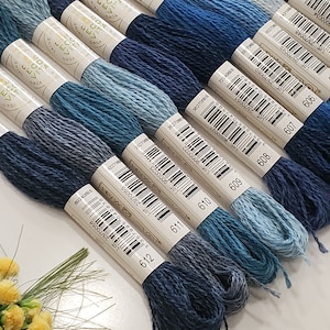 May include: A collection of 10 skeins of DMC embroidery floss in shades of blue, ranging from light to dark. Each skein is labelled with the DMC colour number and a barcode.