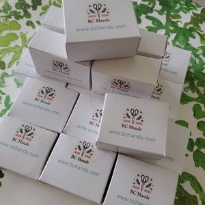 May include: A stack of white boxes with a logo of scissors and the text "BC Hands" and the website address "www.bchands.com" printed on each box.