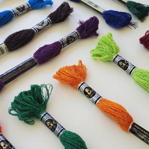 Puede incluir: Surtido de carretes de hilo de bordar DMC en varios colores, incluyendo verde, naranja, rojo, morado y azul. Cada carrete tiene una etiqueta negra con letras doradas que dicen "DMC Special Moulin&eacute; Etoile".